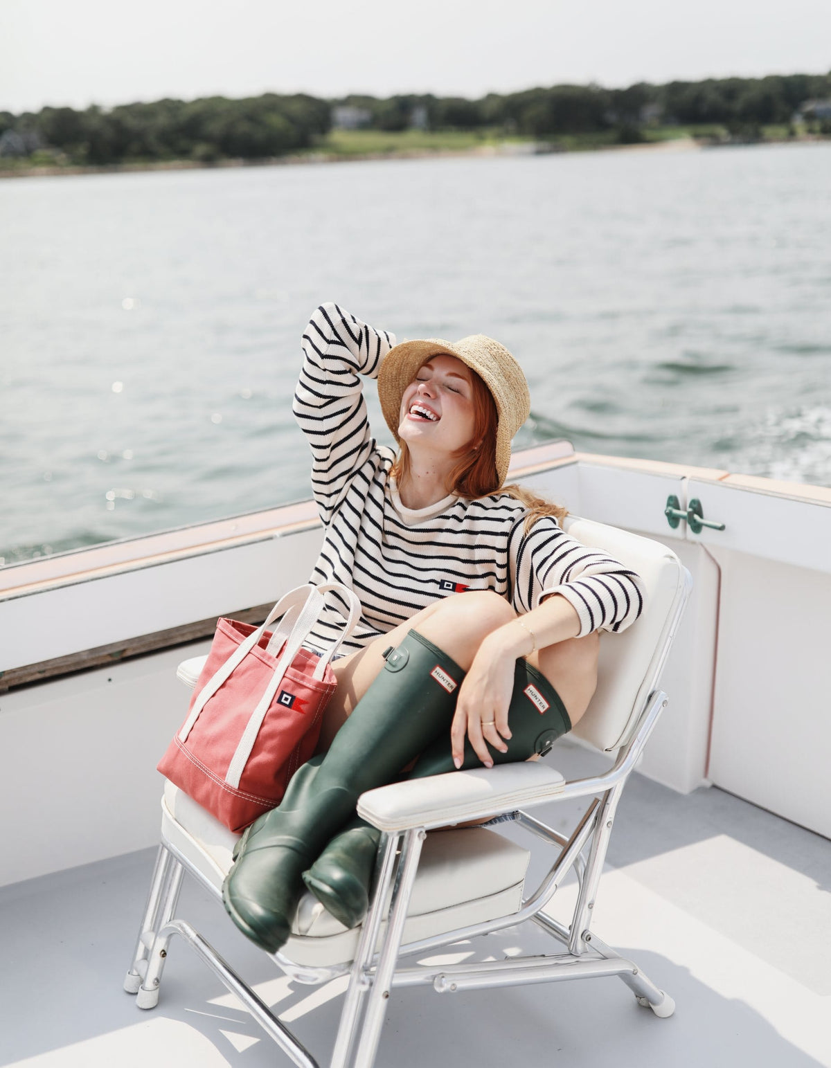 A woman laughing in a boat chair in a Signal Rollneck Sweater with the Signal Mini Tote