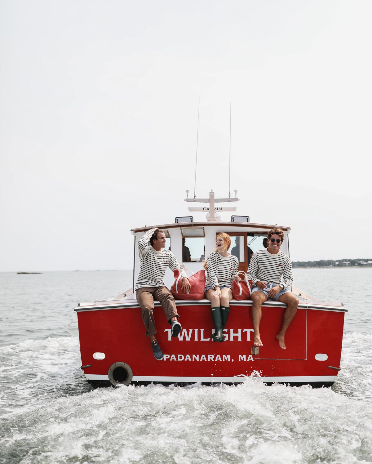 Three people in Signal Rollneck Sweaters on the stern of the red lobster boat Twilight with Signal totes