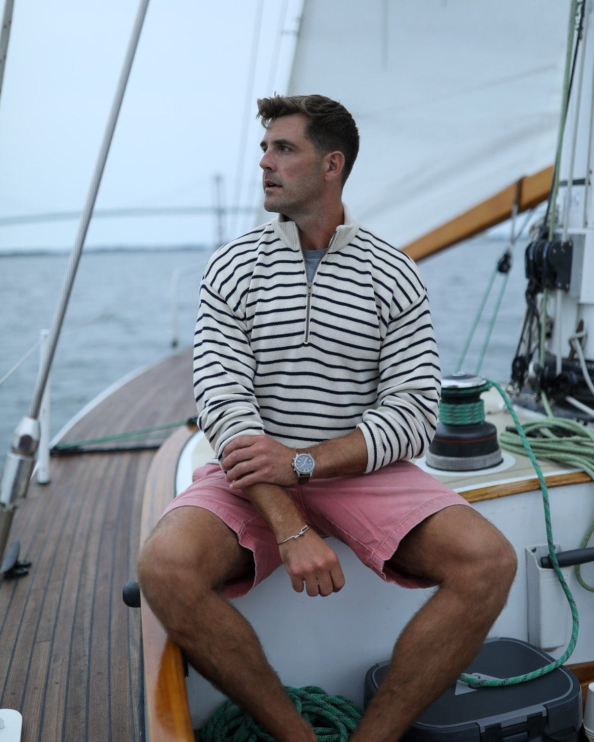 Whalerknits Nantucket Classic 1/4 Zip Sweater: A man in natural with navy stripes and pink shorts sits aboard a sailboat.