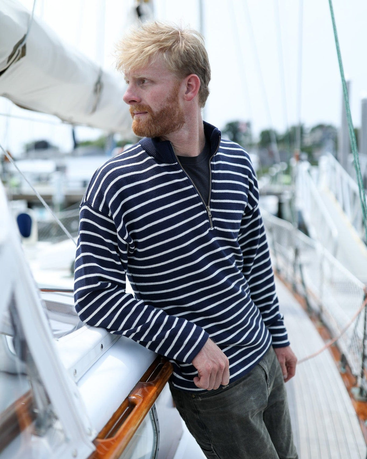 Whalerknits Nantucket Classic 1/4 Zip Sweater: A man in navy with natural stripes leans against the wooden trim of a sailboat.