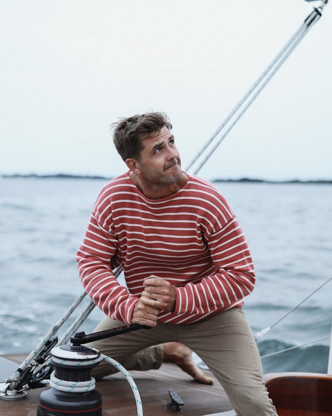 Whalerknits Nantucket Classic Boatneck Sweater: A man in red with natural stripes works a sailboat winch.