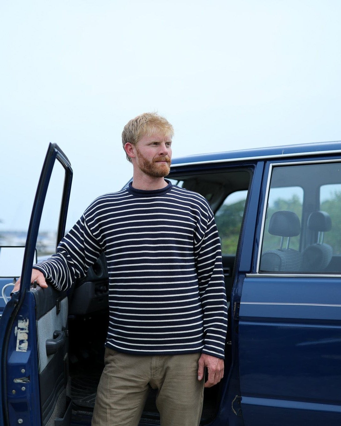 Whalerknits Nantucket Rollneck Sweater: A man in navy with natural stripes stands beside an open blue vehicle door.