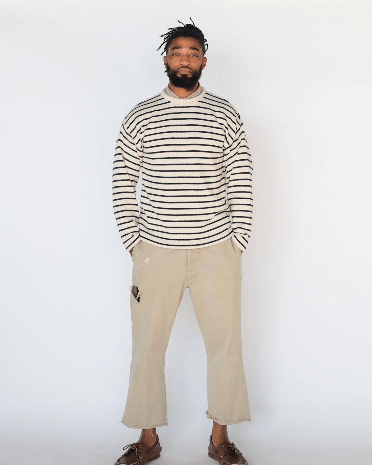 Whalerknits Nantucket Rollneck Sweater: Studio front view of a man wearing natural with navy stripes and light trousers.