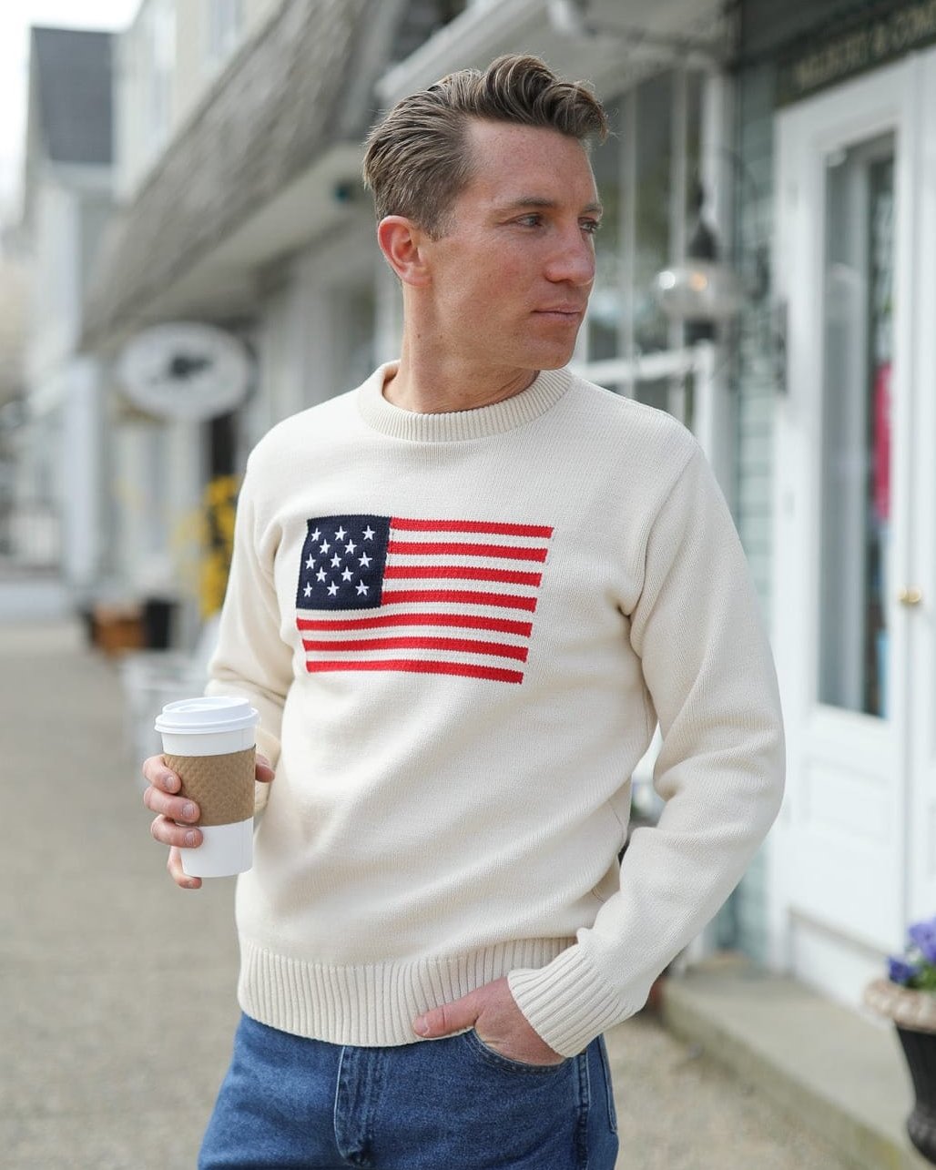 Whalerknits Bristol - American Flag Crewneck: A man wears the natural American flag sweater with jeans while holding a takeaway coffee.