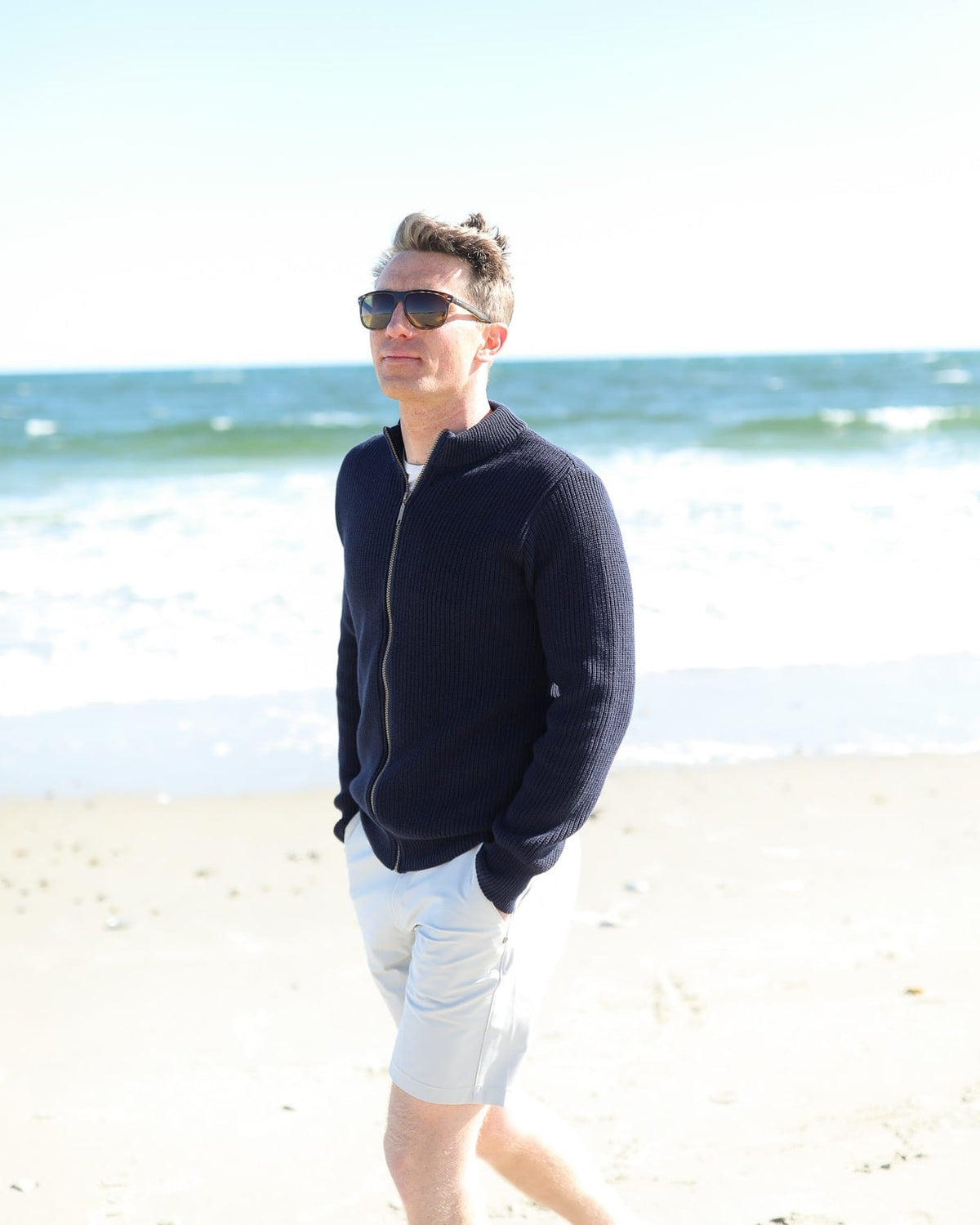 Whalerknits Cuttyhunk Full-Zip Cardigan: A man in navy and light shorts stands on a beach wearing sunglasses.