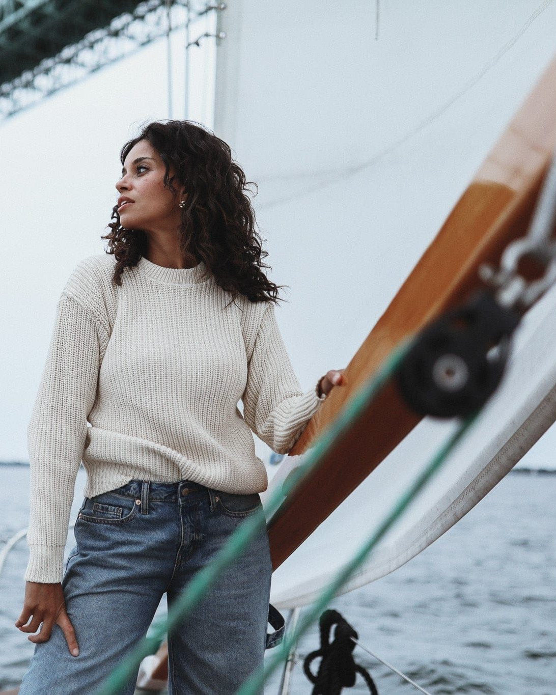Whalerknits Newport Shaker Knit Crewneck Sweater: A woman wears natural with jeans aboard a sailboat, with a bridge behind her.