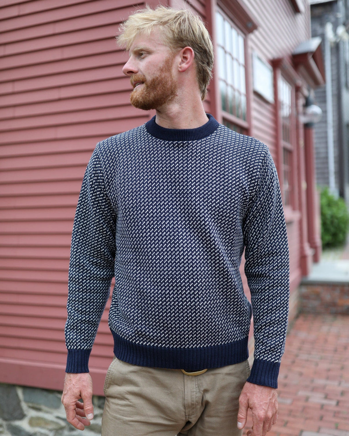 Whalerknits Sakonnet Birdseye Crewneck Pullover: A man in navy with natural birdseye pattern stands beside a red house.