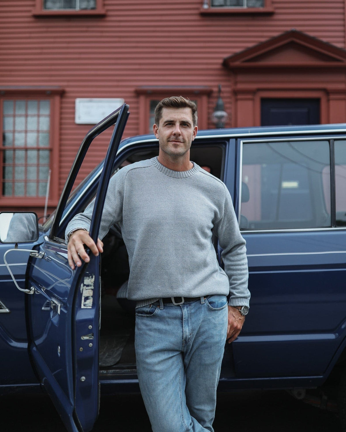 Whalerknits Westport Crewneck Saddle Shoulder Pullover: A man in the light fine-striped sweater and jeans leans on an open blue vehicle door.