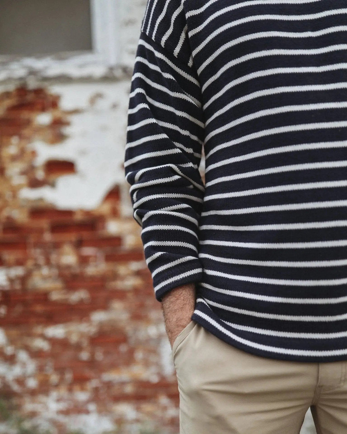 Whalerknits Nantucket Classic Boatneck Sweater: Close-up of a navy and natural striped sweater worn with tan trousers beside a brick wall.