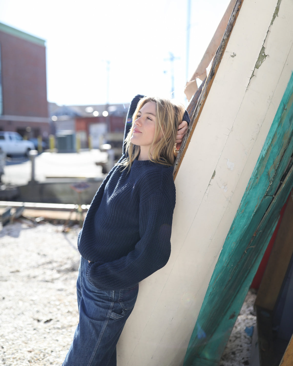 Whalerknits Newport Shaker Knit Crewneck Sweater: A woman in navy and jeans leans against a weathered white and turquoise boat hull.