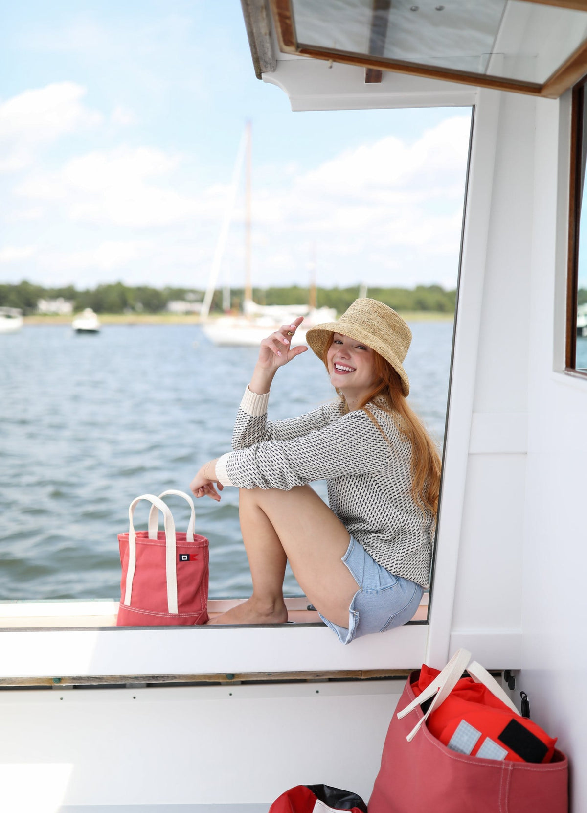 A woman in a straw hat sits in the boat's cabin door beside the Signal Mini Tote