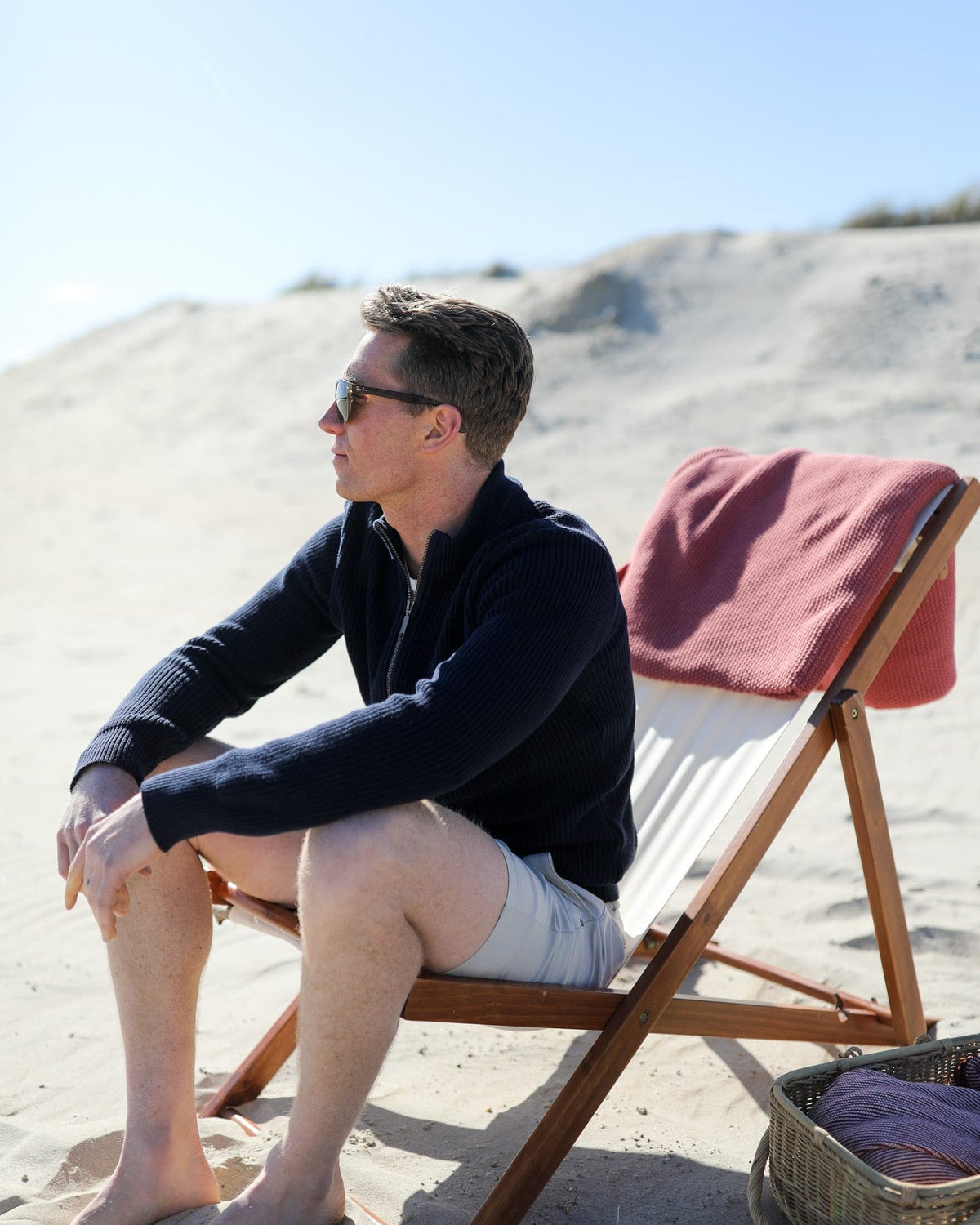 Whalerknits Cuttyhunk Full-Zip Cardigan: A man in navy and light shorts sits in a wooden beach chair.