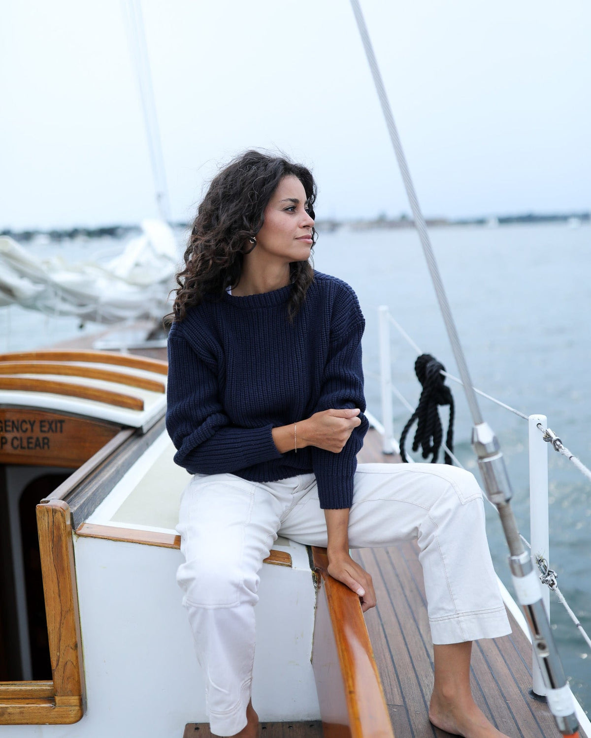 Whalerknits Newport Shaker Boatneck Sweater: A woman in navy and white trousers sits beside a sailboat companionway.