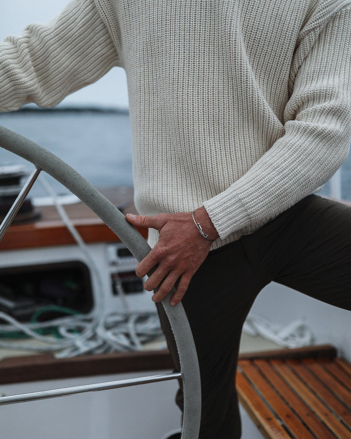 Whalerknits Newport Shaker Knit Crewneck Sweater: Close view of a natural-colored sweater worn by a person holding a sailboat wheel.
