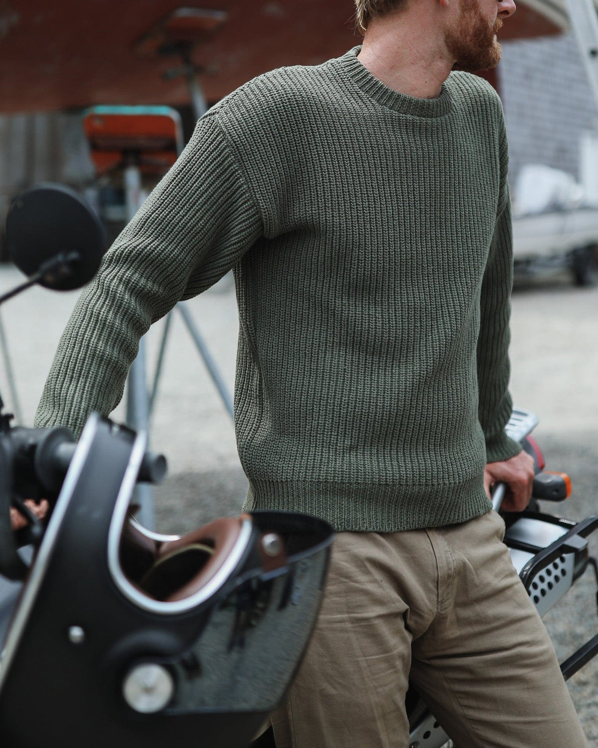 Whalerknits Newport Shaker Knit Crewneck Sweater: A man wears olive with tan trousers beside boat equipment, showing the ribbed body and cuffs.