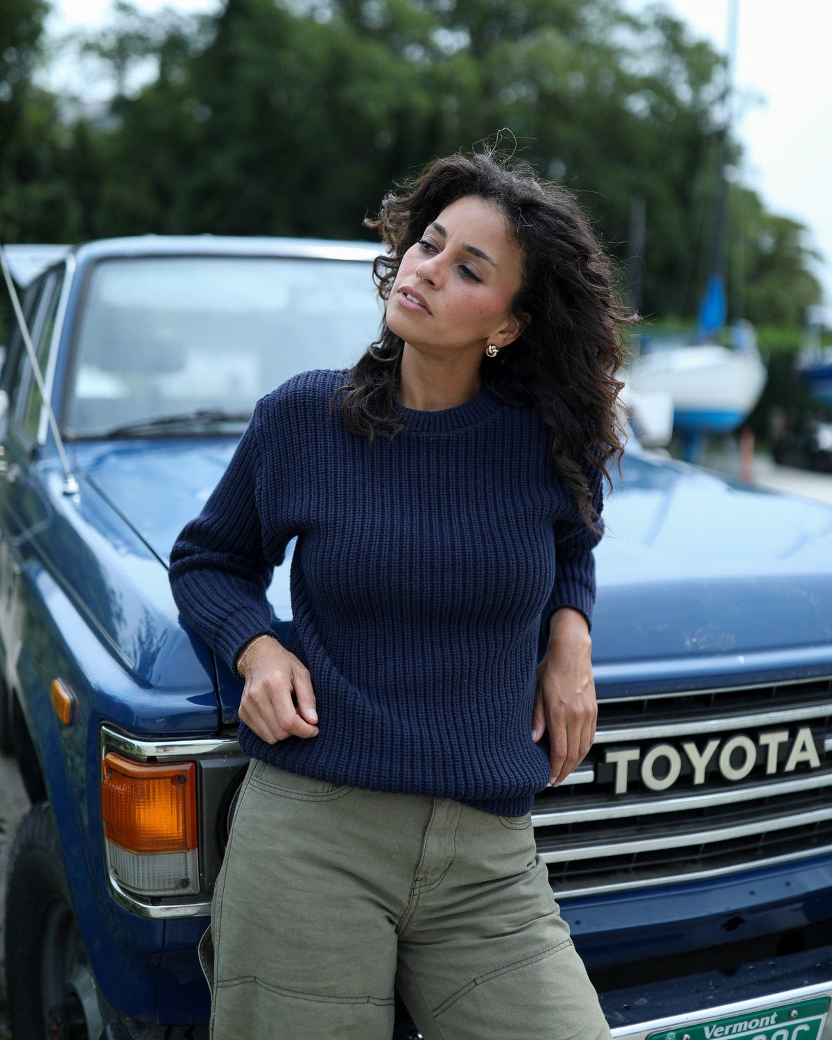 Whalerknits Newport Shaker Knit Crewneck Sweater: A woman in navy with olive trousers leans against the front of a blue Toyota.