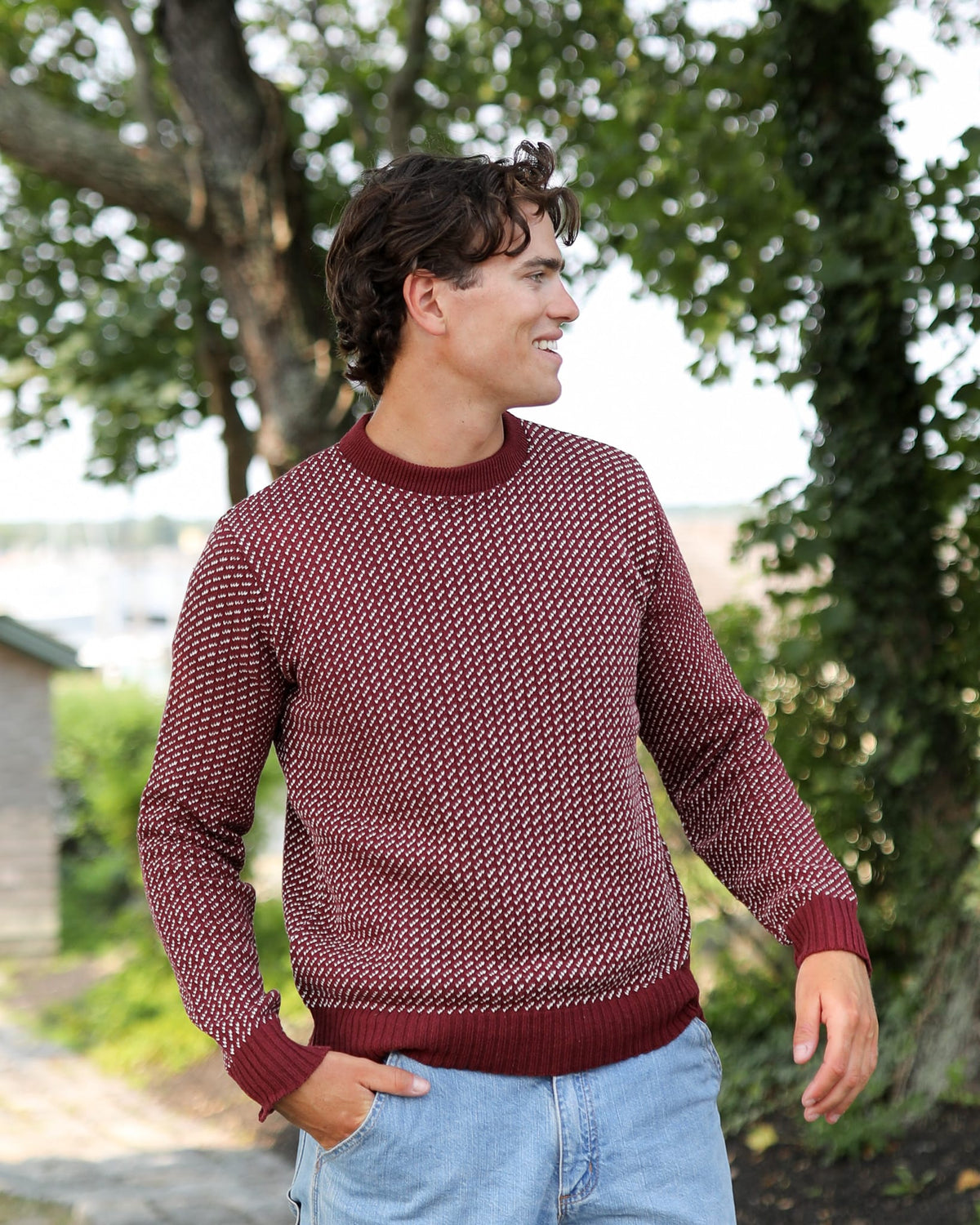 Whalerknits Sakonnet Birdseye Crewneck Pullover: A man wears burgundy with natural birdseye pattern and jeans outdoors.