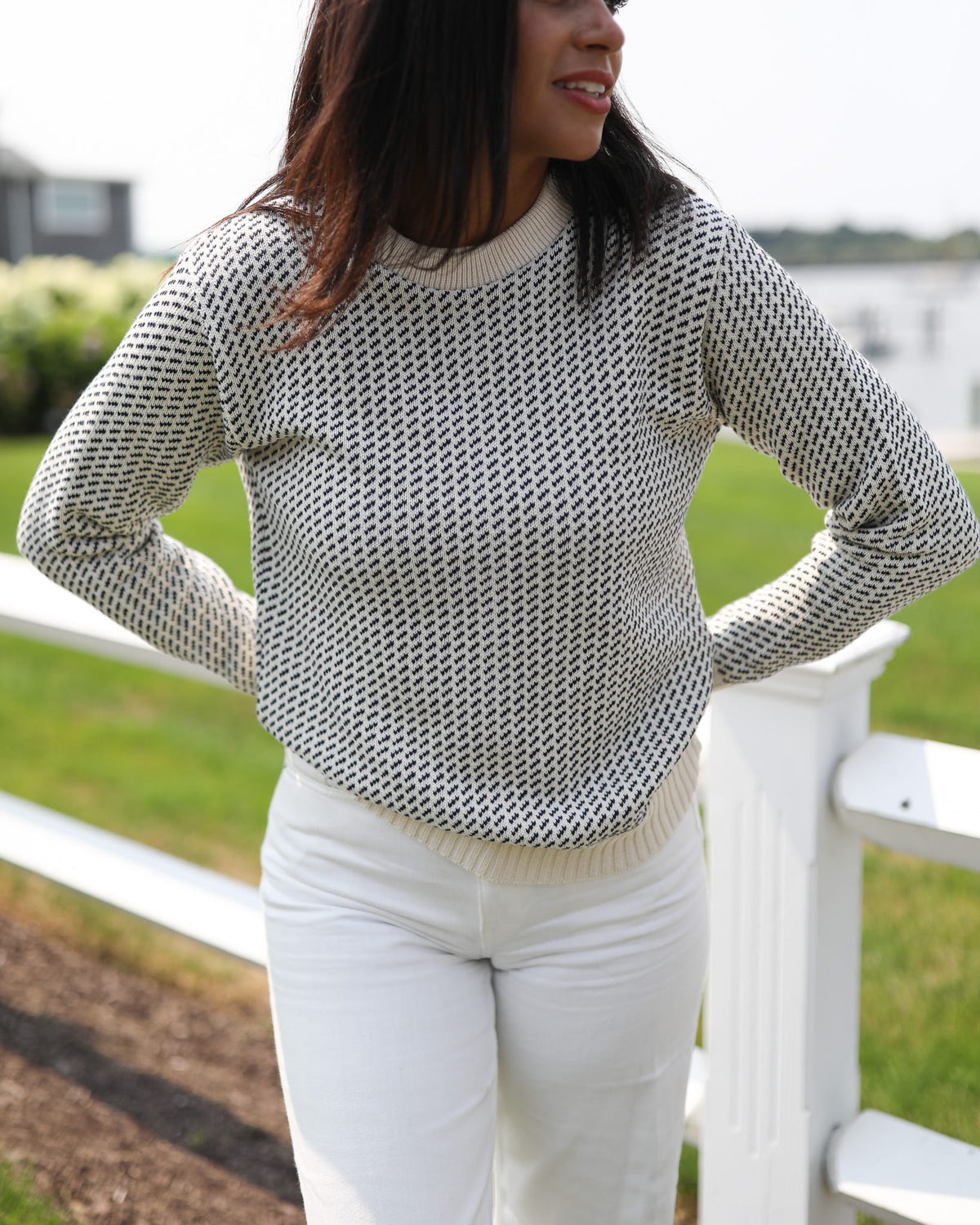Whalerknits Sakonnet Birdseye Crewneck Pullover: Close view of a woman wearing natural with navy birdseye pattern and white trousers beside a white fence.