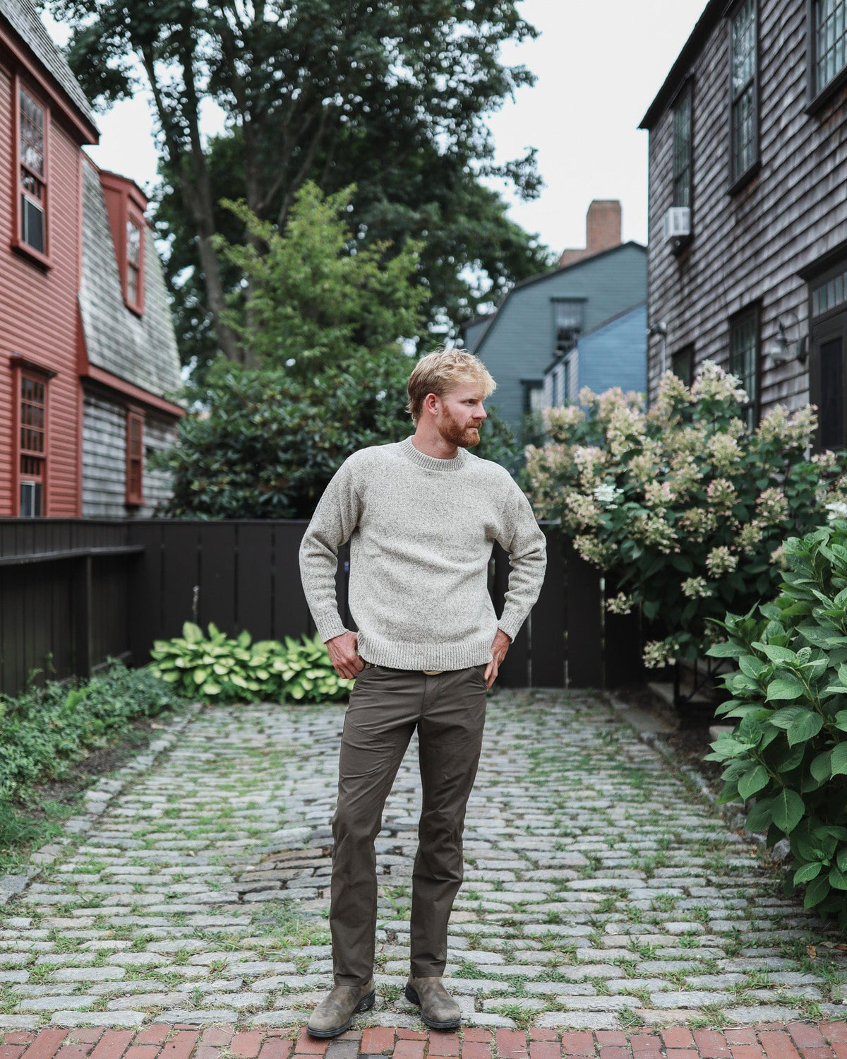 Whalerknits Wellfleet Classic Crewneck Jersey - Wool Blend: Full-length view of a man in the light sweater and dark trousers standing on a cobbled path.