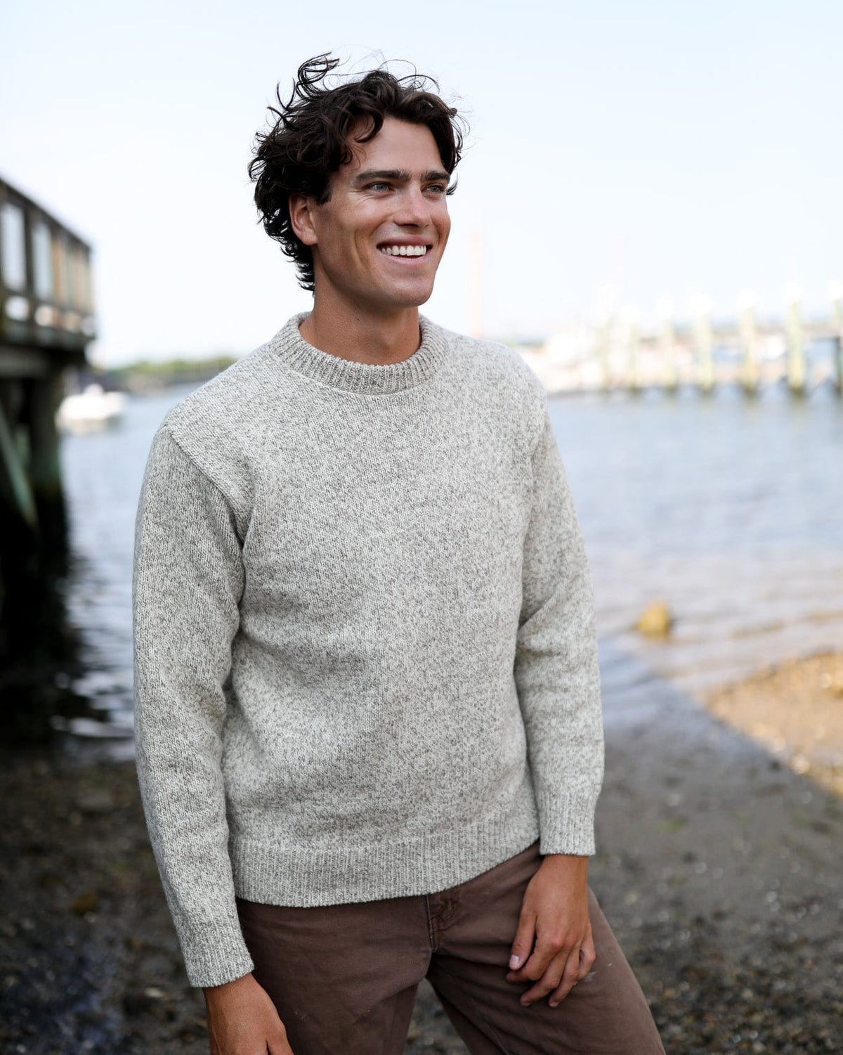Whalerknits Wellfleet Classic Crewneck Jersey - Wool Blend: A smiling man wears the light heathered sweater beside a harbor.