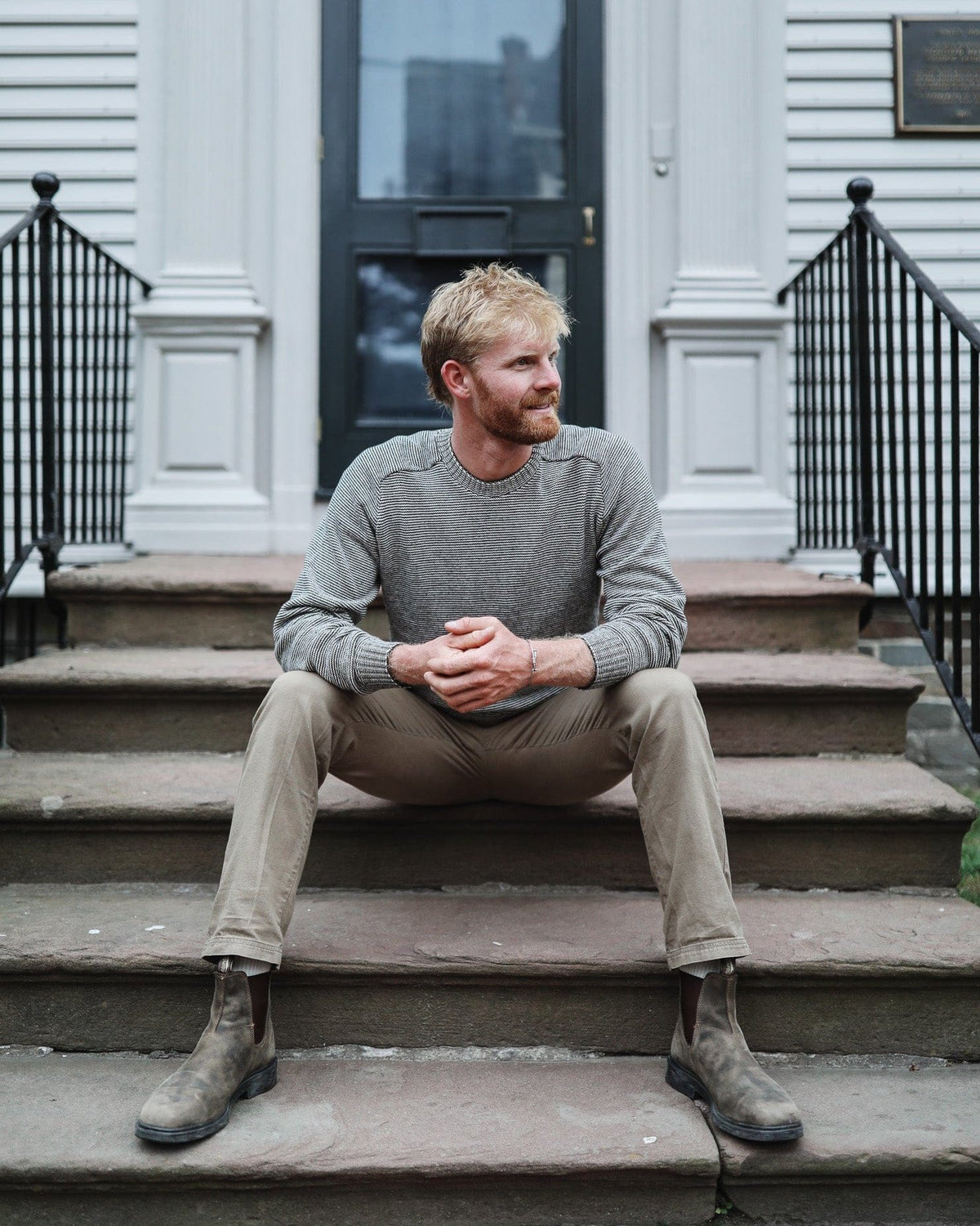 Whalerknits Westport Crewneck Saddle Shoulder Pullover: A man in the gray fine-striped sweater and tan trousers sits on stone steps.