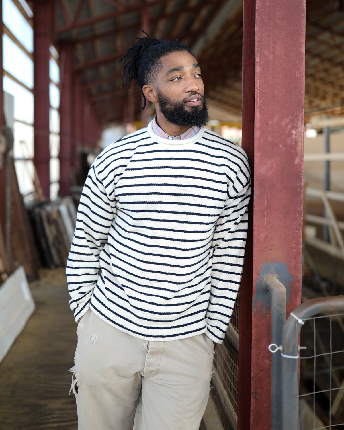 Whalerknits Nantucket Rollneck Sweater: A man wears natural with navy stripes and light trousers beside a red workshop post.